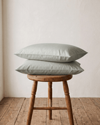 Two RUIE percale pillowcases in sage on a wooden stool